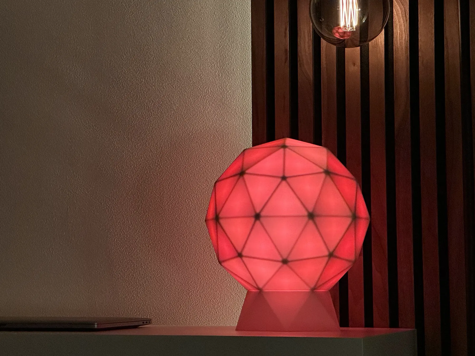A GLORB lit red on a sideboard beside a pendant bulb