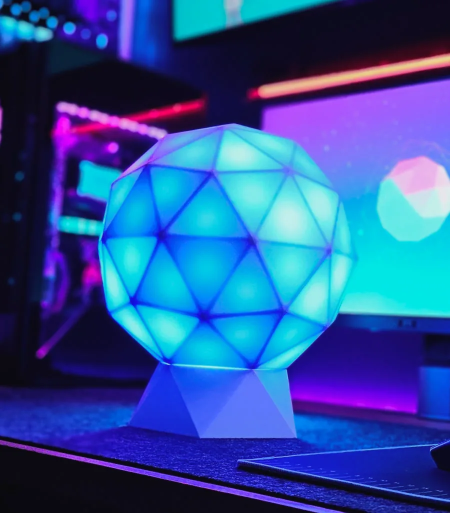 GLORB lit cyan on a gaming desk beside an RGB PC and monitor