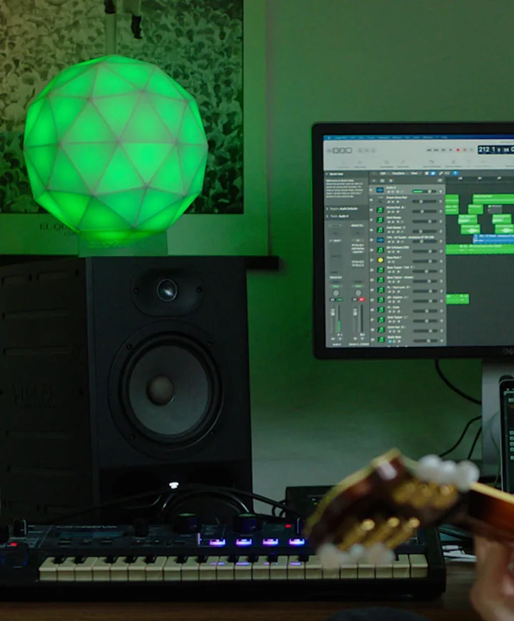 GLORB lit green in a home music studio beside a monitor and keyboard